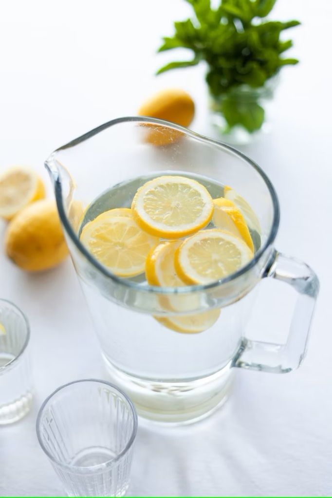 Une carafe et deux verres transparents remplis d'eau infusée au citron pour une bonne hydration l'été.